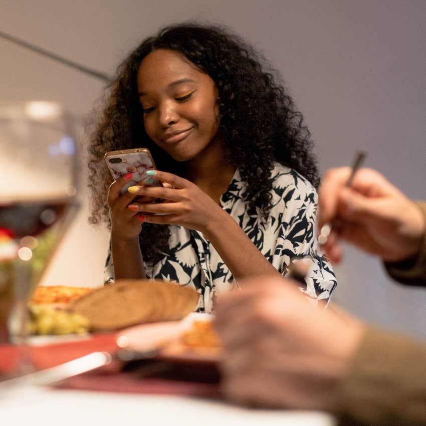 gen Z woman with bad table manners using her phone at dinner