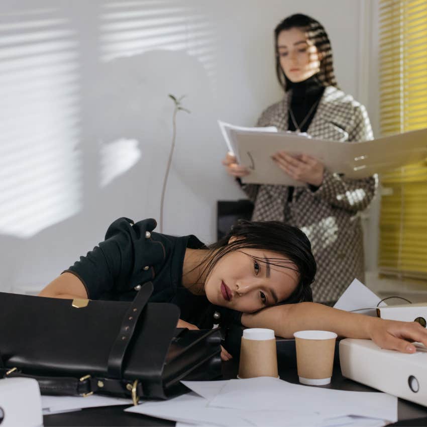 Exhausted employee sitting at a desk surrounded by work while feeling overwhelmed