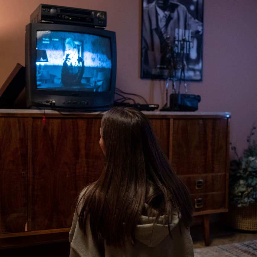 Teenager sitting near a television and VCR while rewinding a VHS movie before returning it