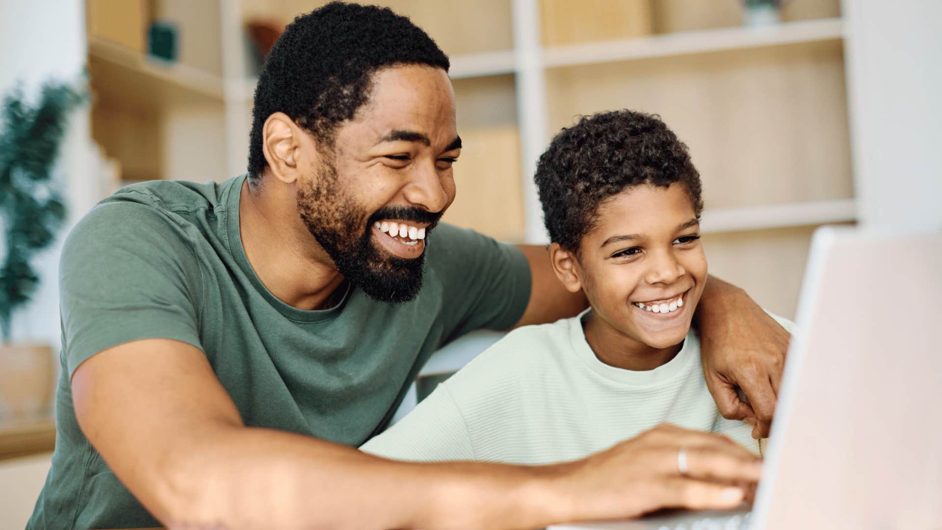 man in green shirt helping son with homework as he says let me do it for you