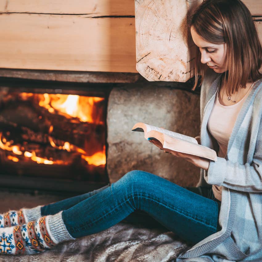 woman enjoying her cozy small house reading book near fireplace