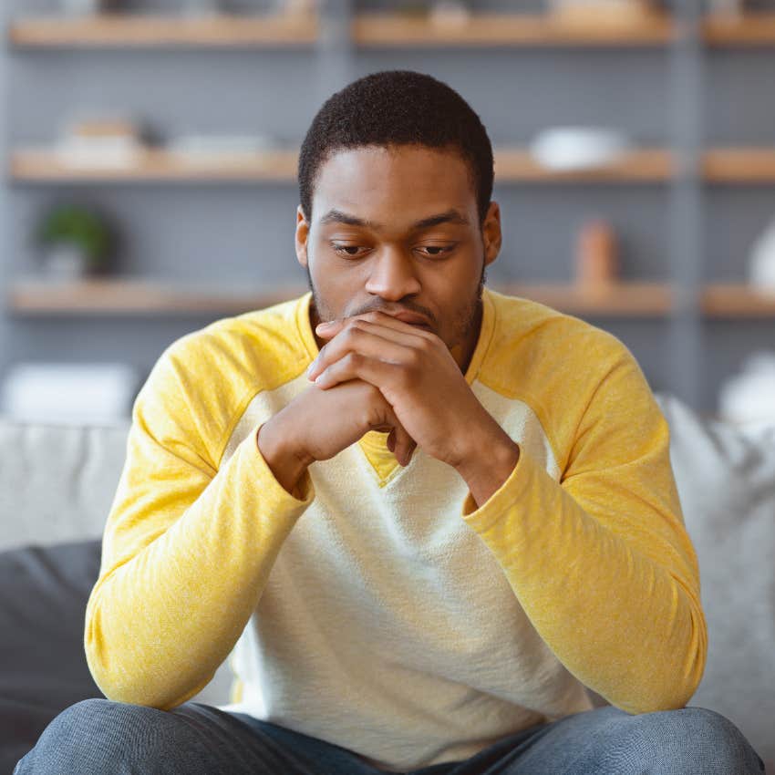 man who keeps others at a distance sitting on the couch looking sad
