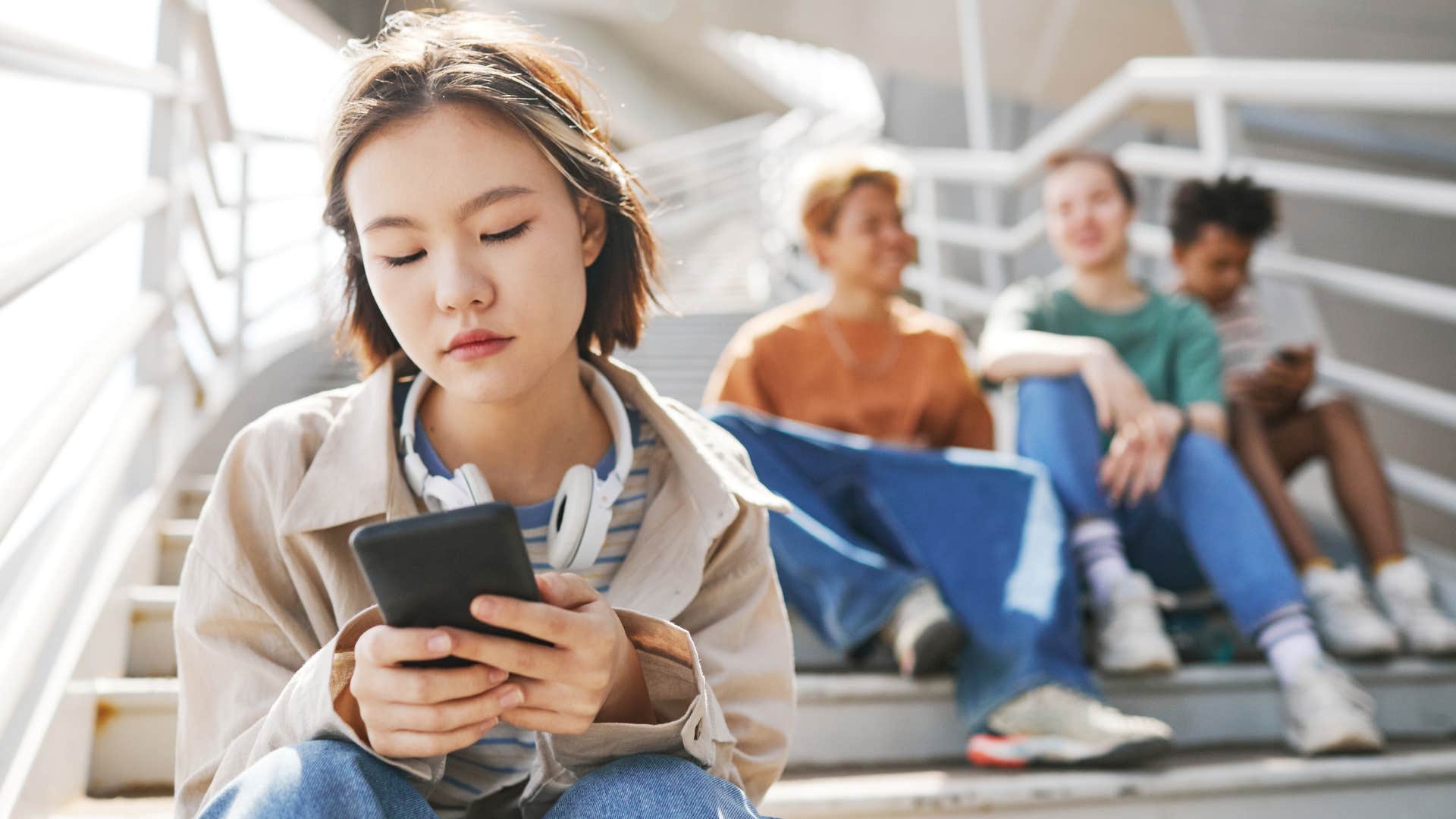 teen girl looking at phone avoiding other kids because she has a hard time trusting