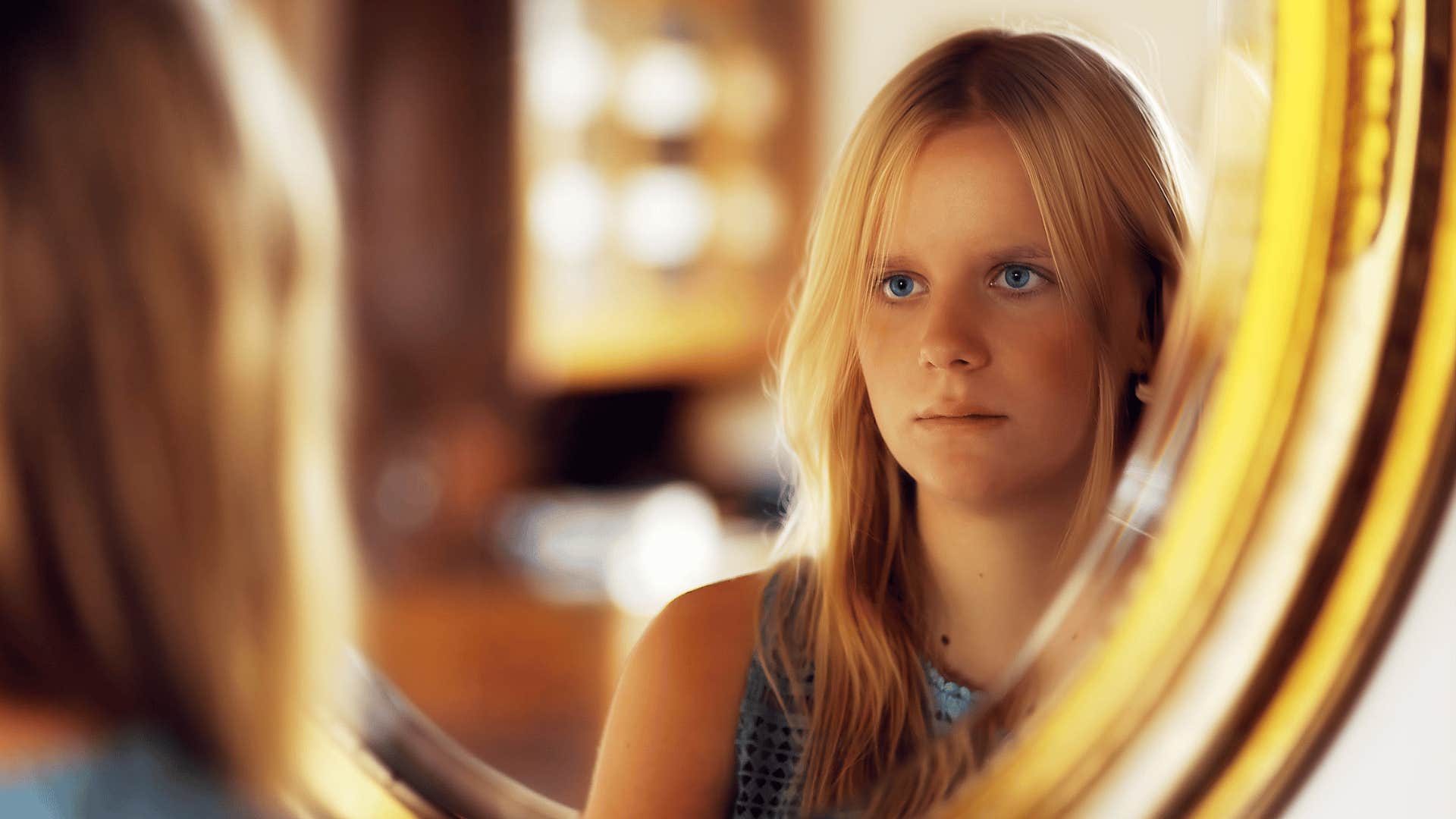 self-critical woman looking in mirror thinking about her upbringing
