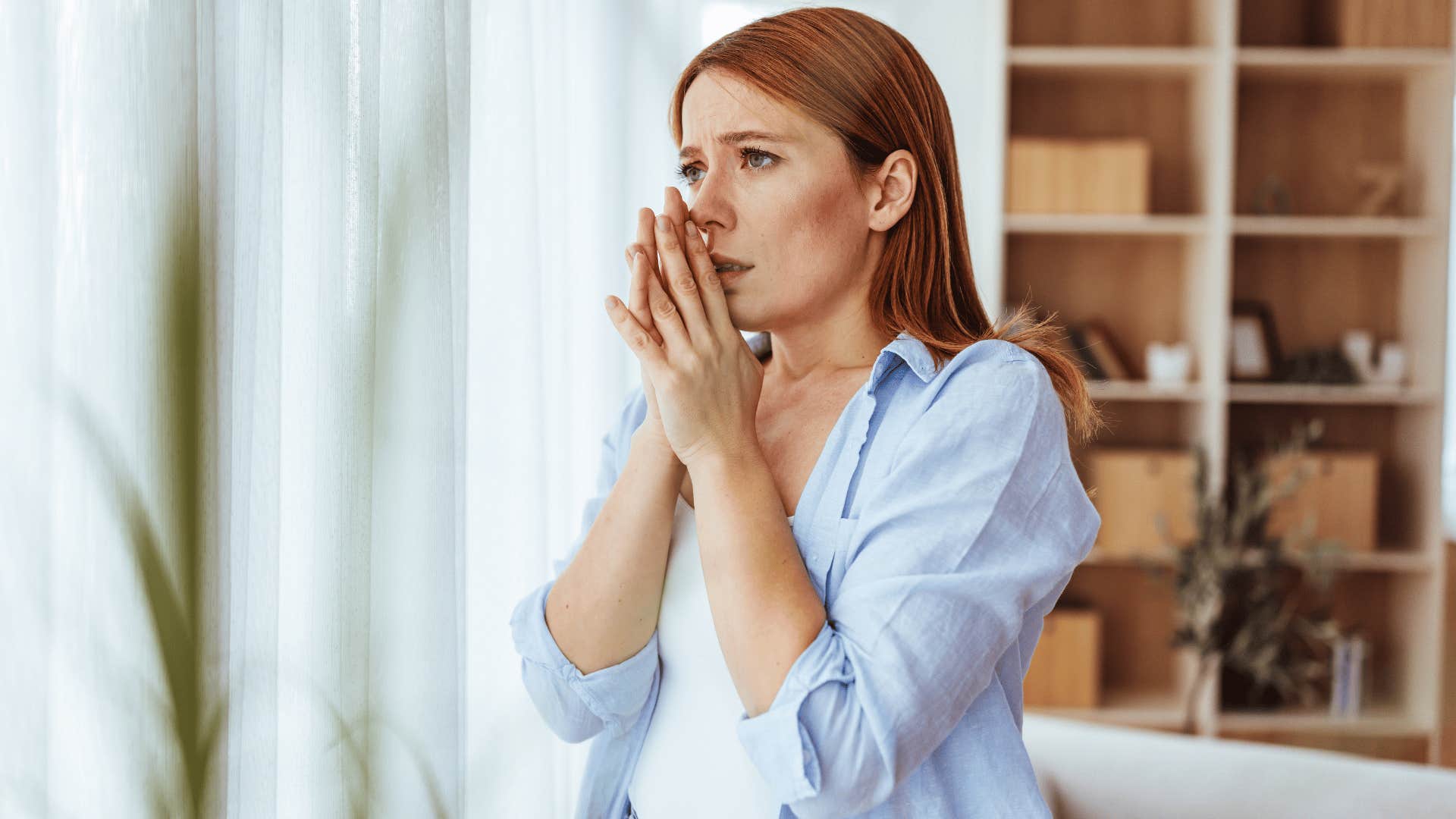 woman looking out the window scared as they avoid taking risks