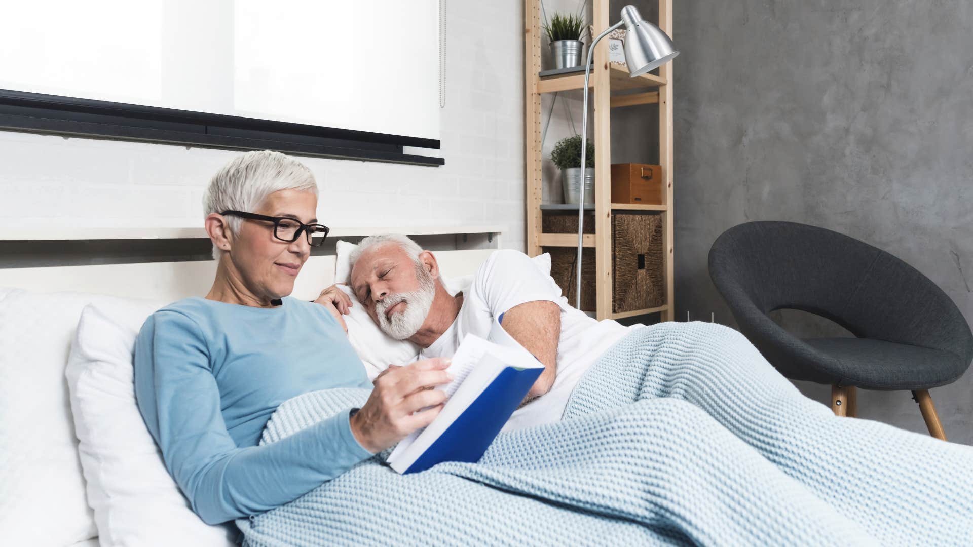 boomer couple in bed wife reading husband sleeping don't have the same sleep schedule