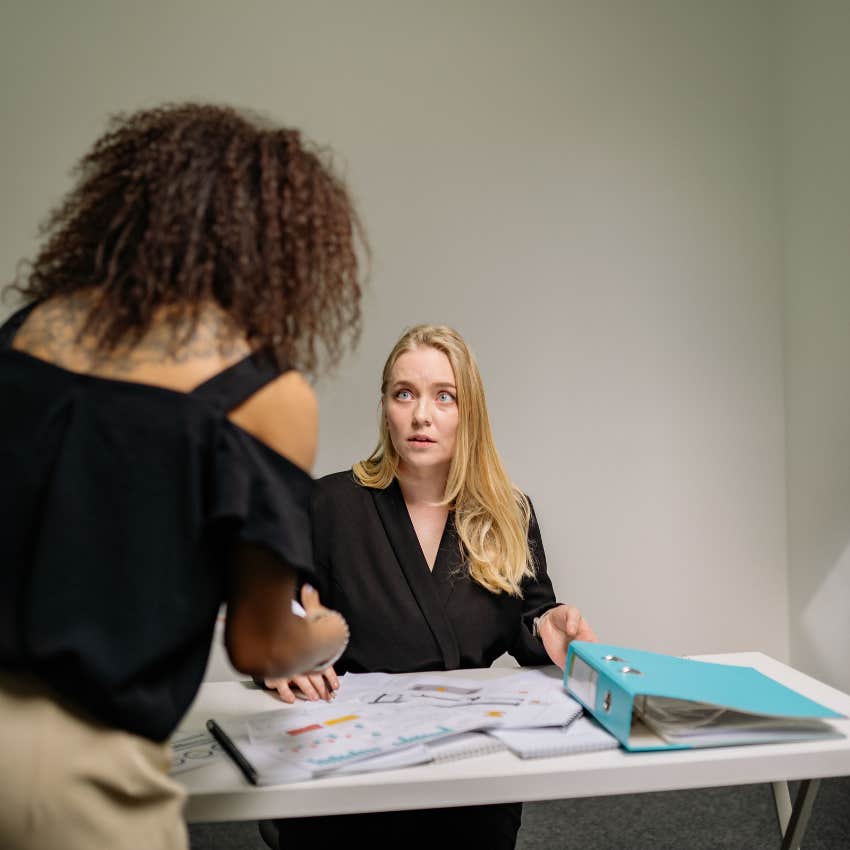 Coworker pointing out an error to a visibly embarrassed employee during a workplace conversation