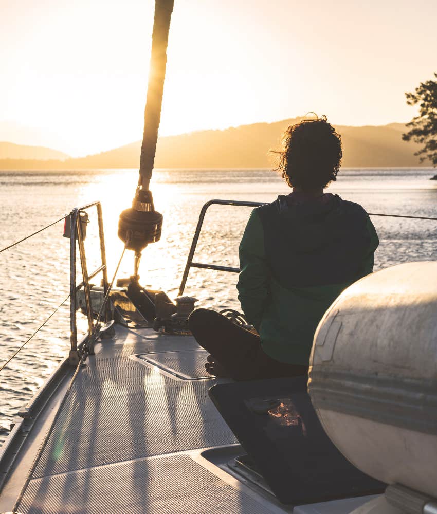 woman on a sailboat looking out at a sunset in silhouette 