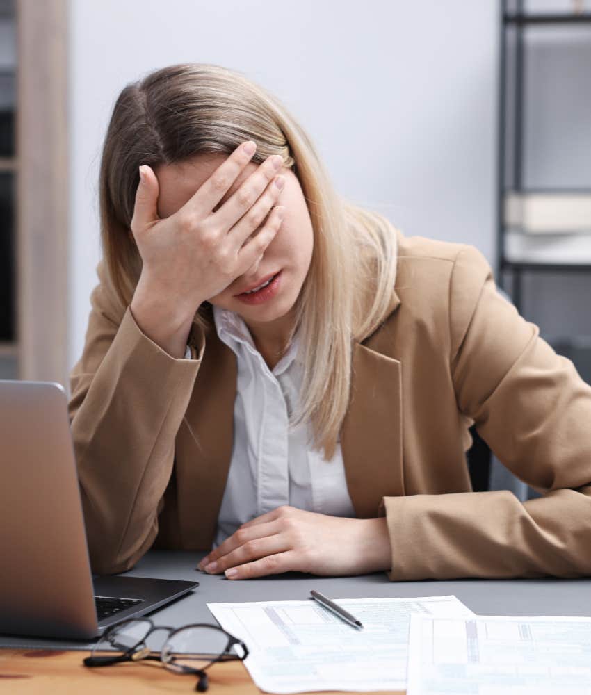 woman who feels emotionally overwhelmed puts her head in her hand at work