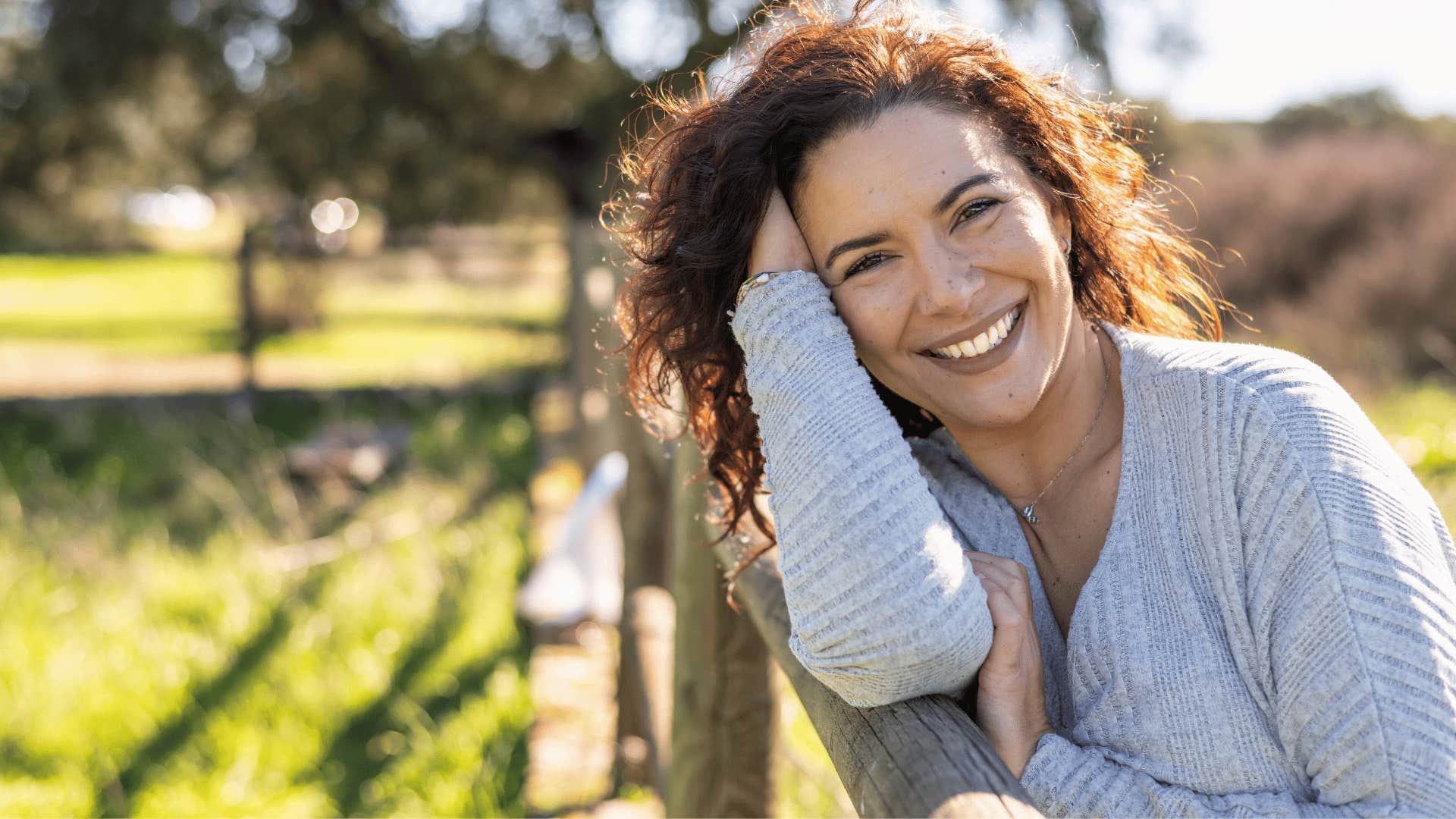 woman in gray sweater smiling outside as she thinks i'm good with what i got