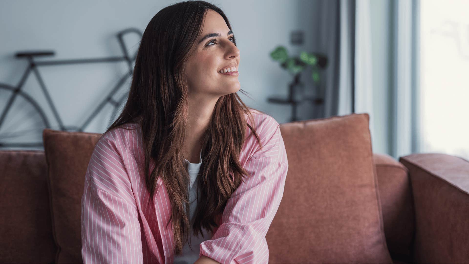 woman in pink shirt smiling brightly on couch as she thinks i don't need to be the best at everything
