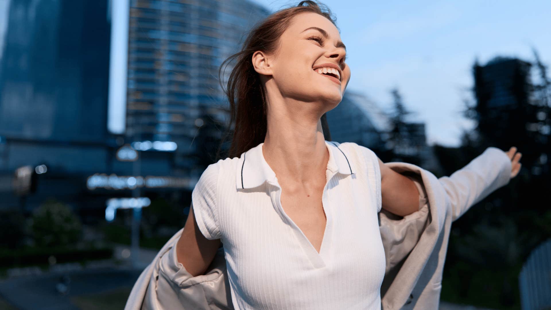 woman in white shirt smiling brightly in city as she thinks people can think what they want