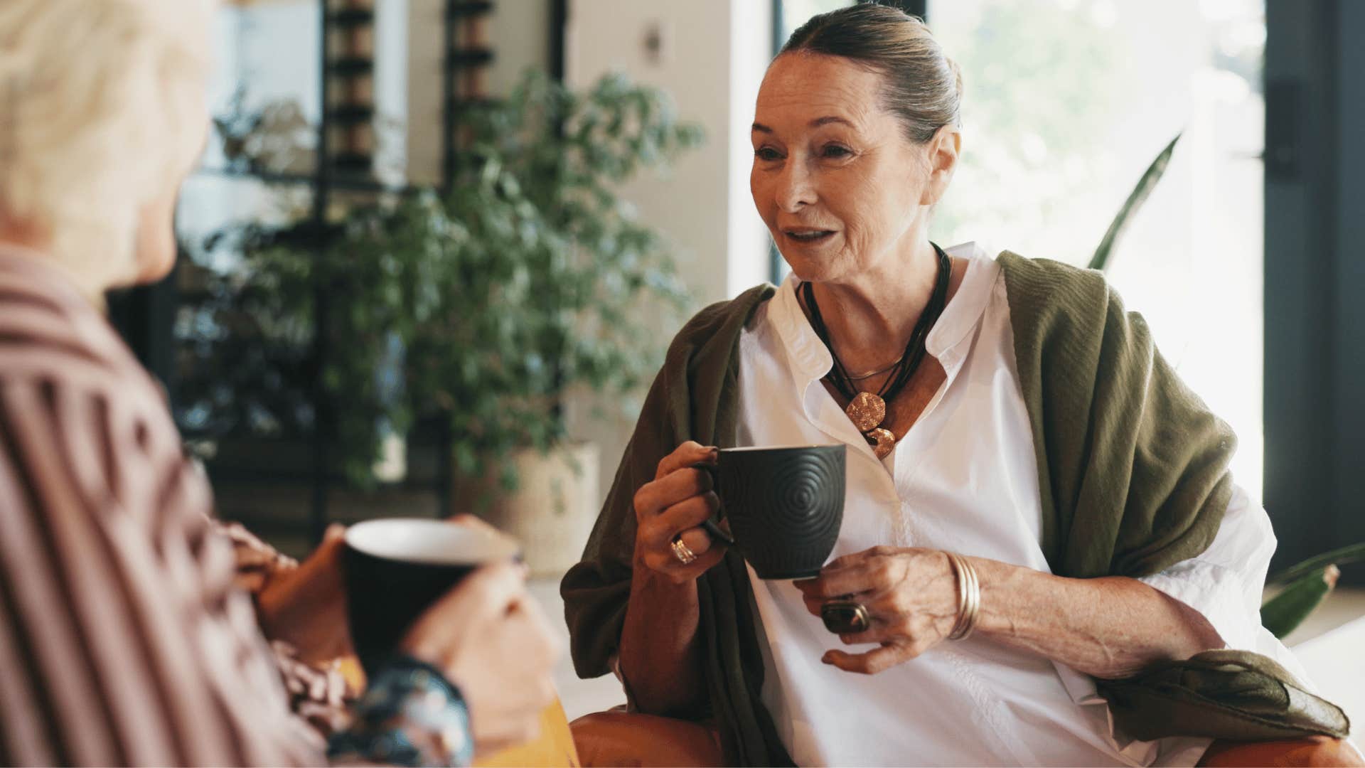 woman in green cardigan drinking tea as she tells friend everyone does it