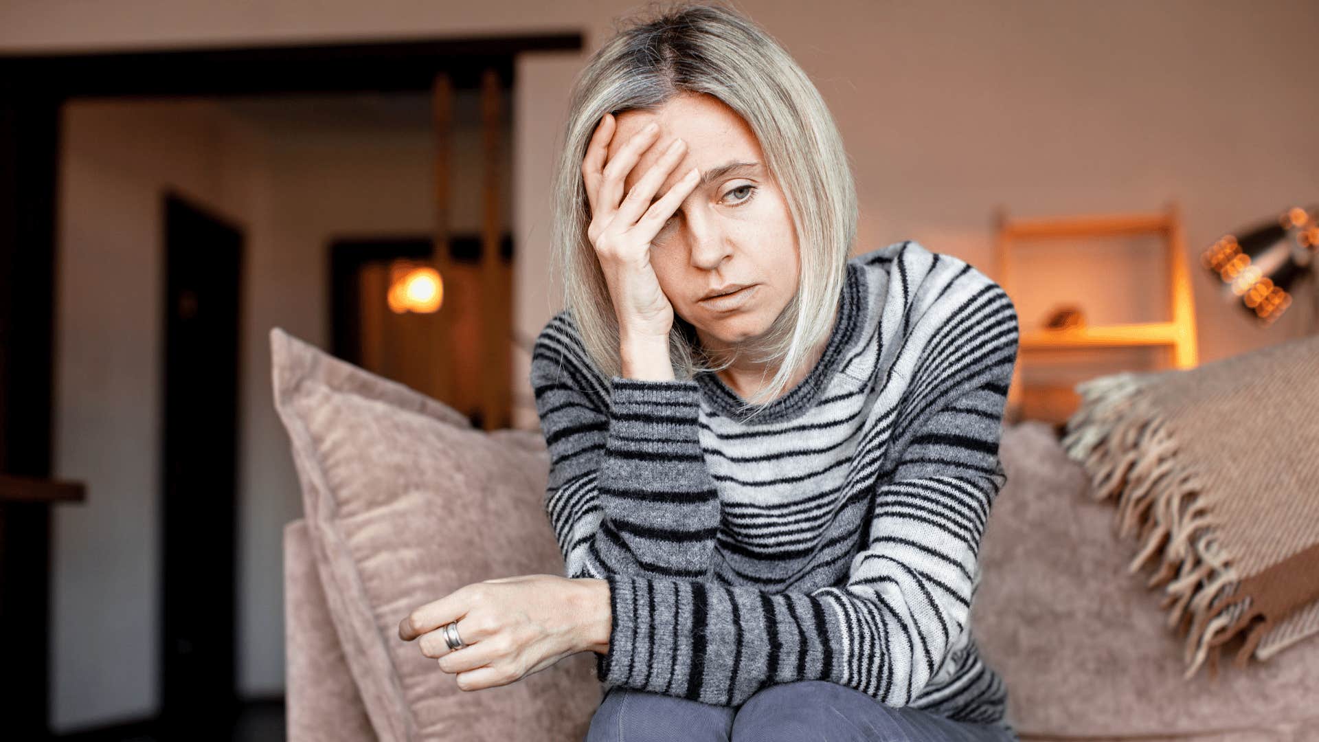woman in stripped shirt thinking i don't want to think about it as she sits on couch