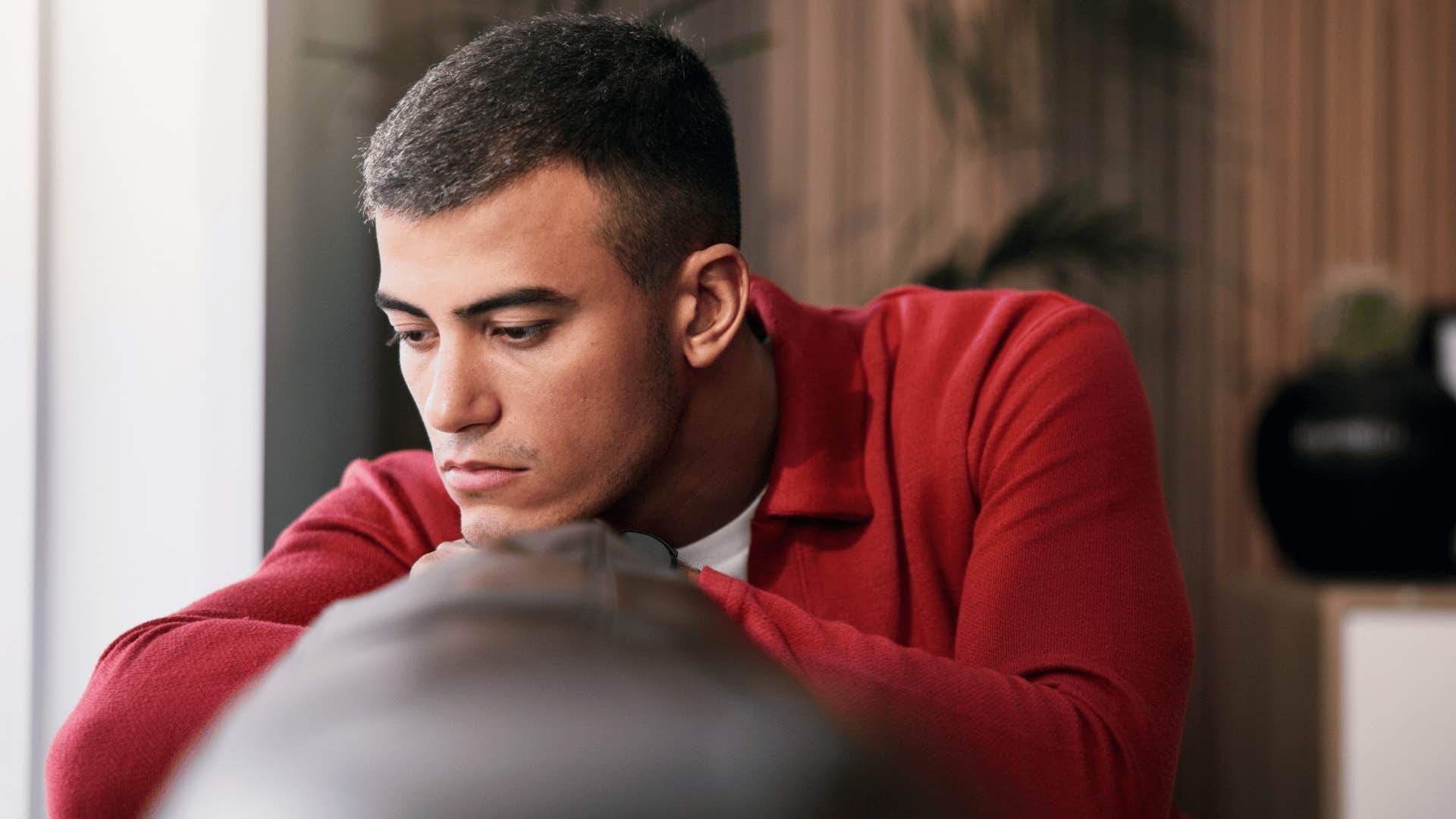 man in red shirt thinking it's not fair while he sits and reflects on couch