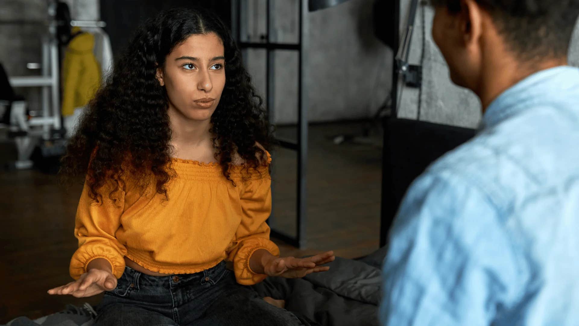 woman in orange shirt holding up hands as she tells man let's break this down