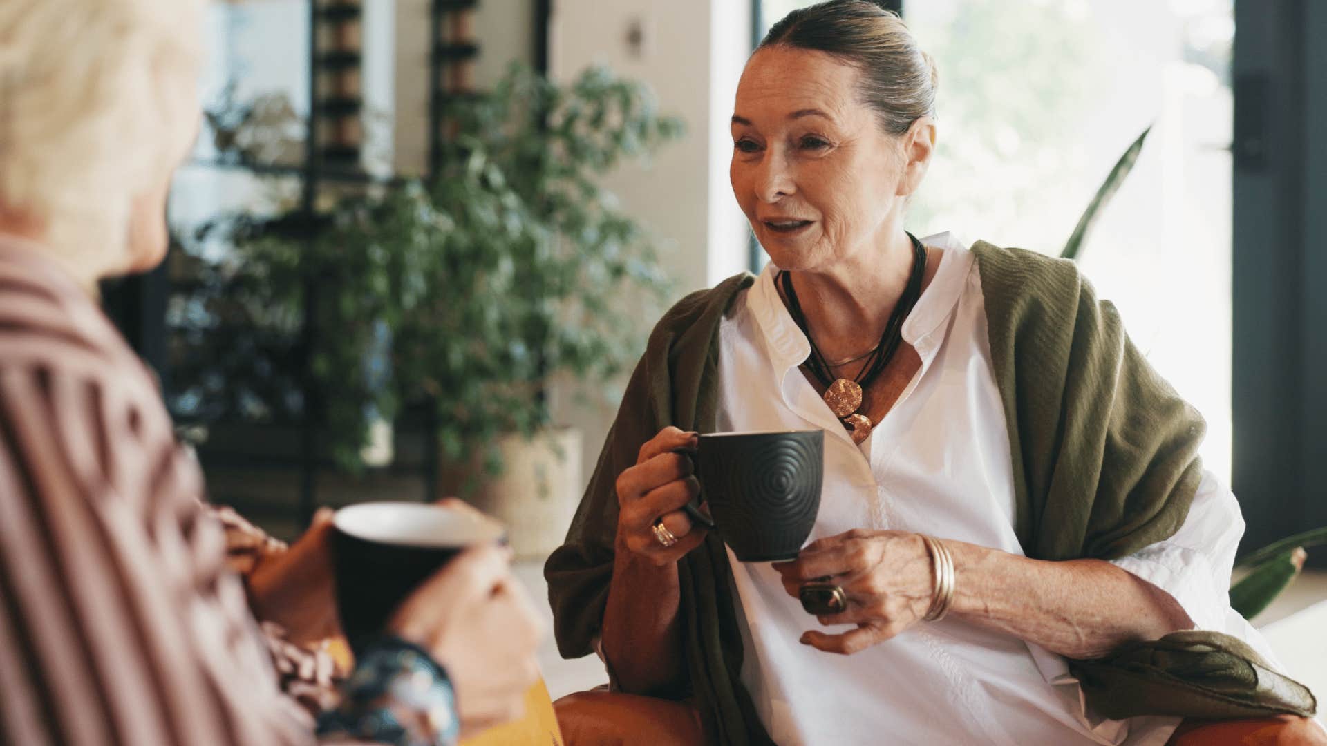 woman in green jacket sipping tea as she tells friend i would never do something like that