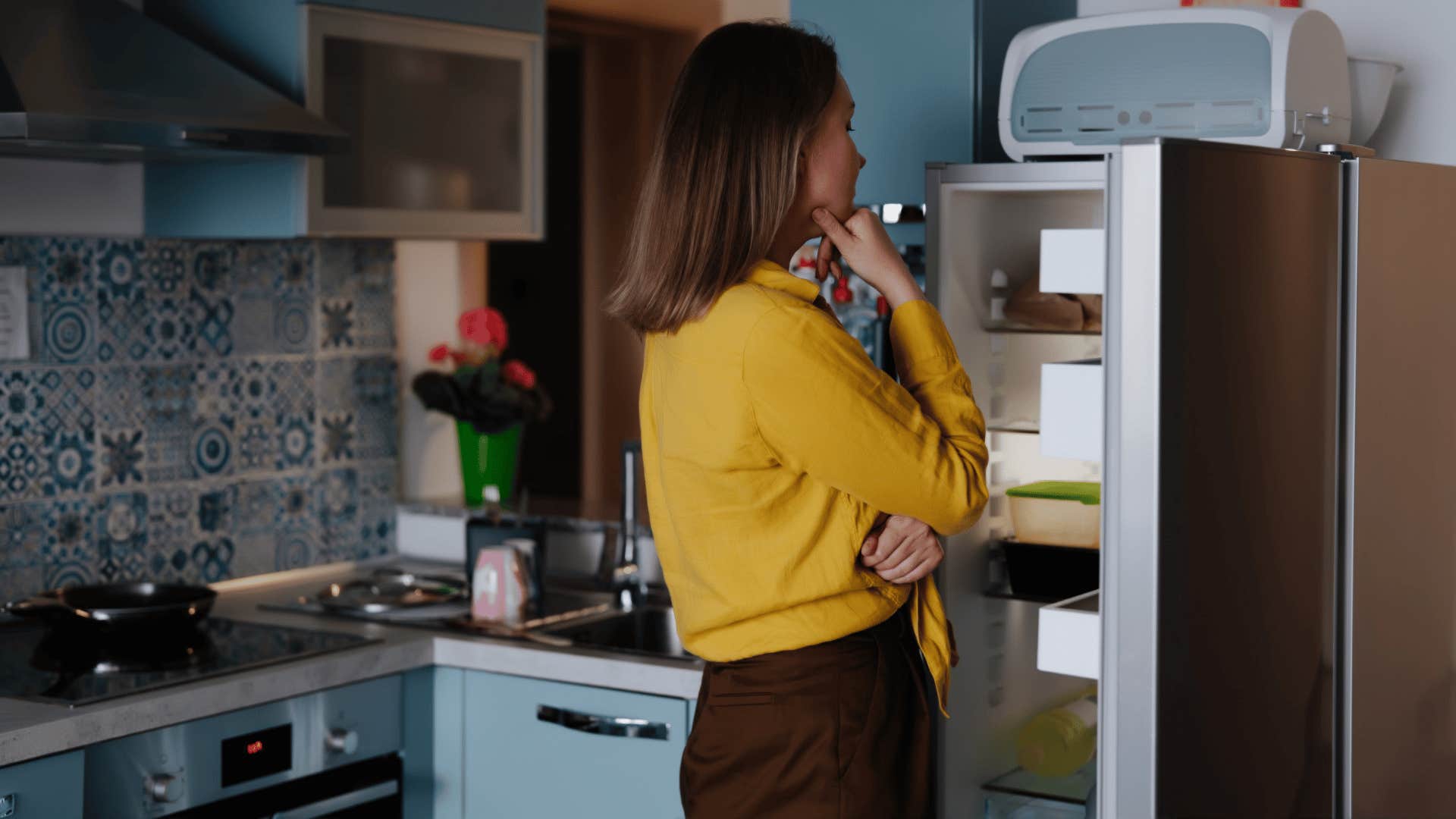 woman in yellow shirt staring at the fridge thinking i'm trying to make what i have last