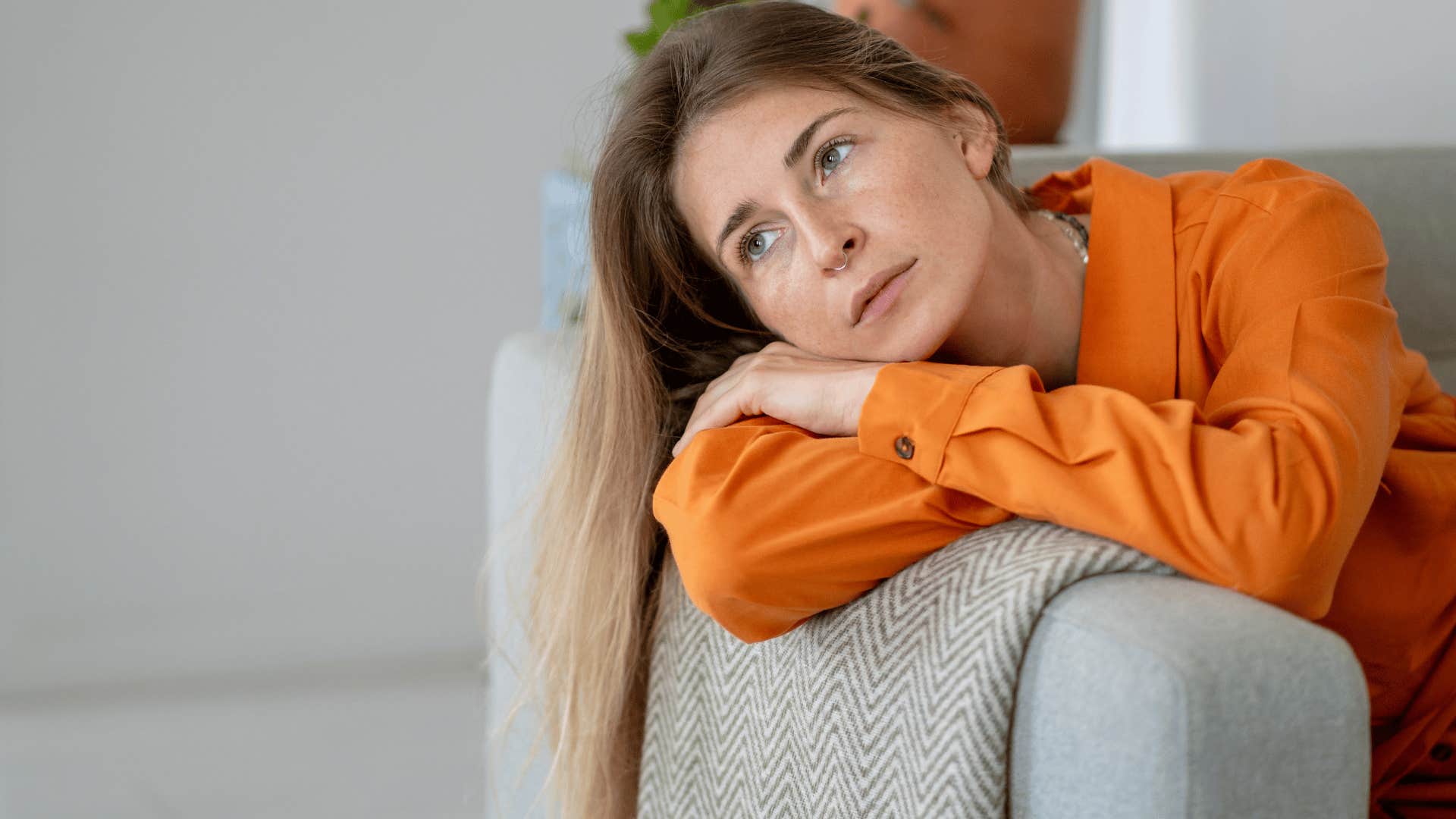 woman in orange shirt thinking i don't have the energy for much as she lays on couch