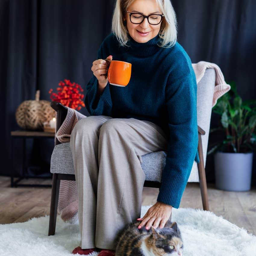 woman thrilled fall is coming petting her cat while sipping coffee and prioritizing her comfort