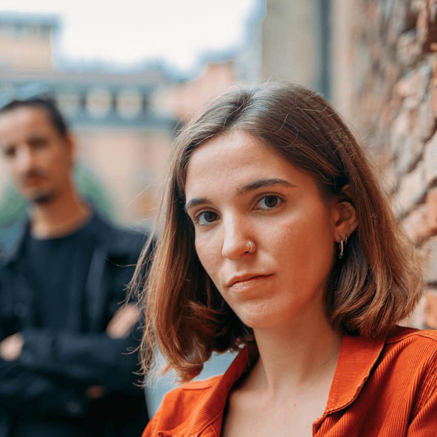 young woman with a serious expression with a man in the background