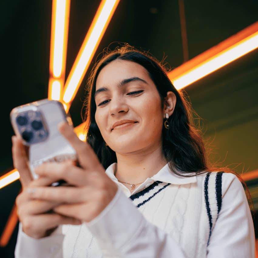 young woman smiling down at her phone mentally obsessed