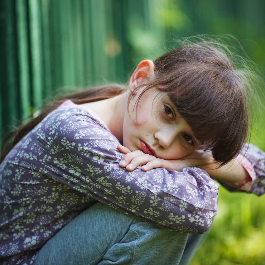 little girl who is a good kid crouching outdoors and thinking 