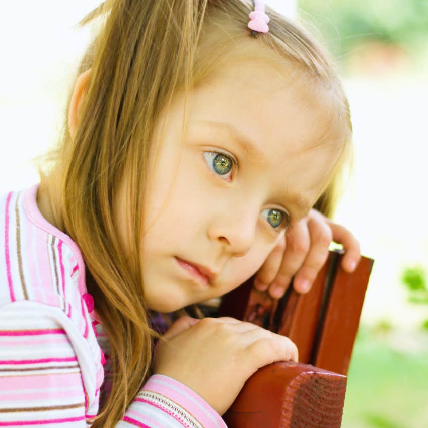 little girl who is a good kid looking sadly over a fence