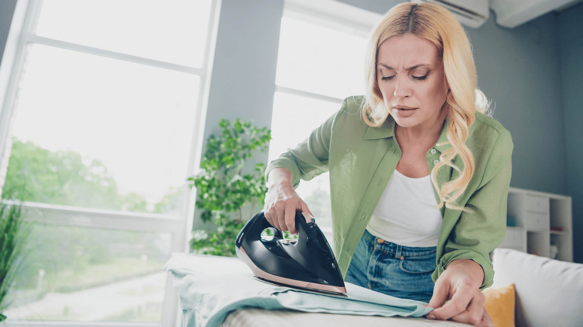 woman in green cardigan ironing their everyday clothes before wearing them