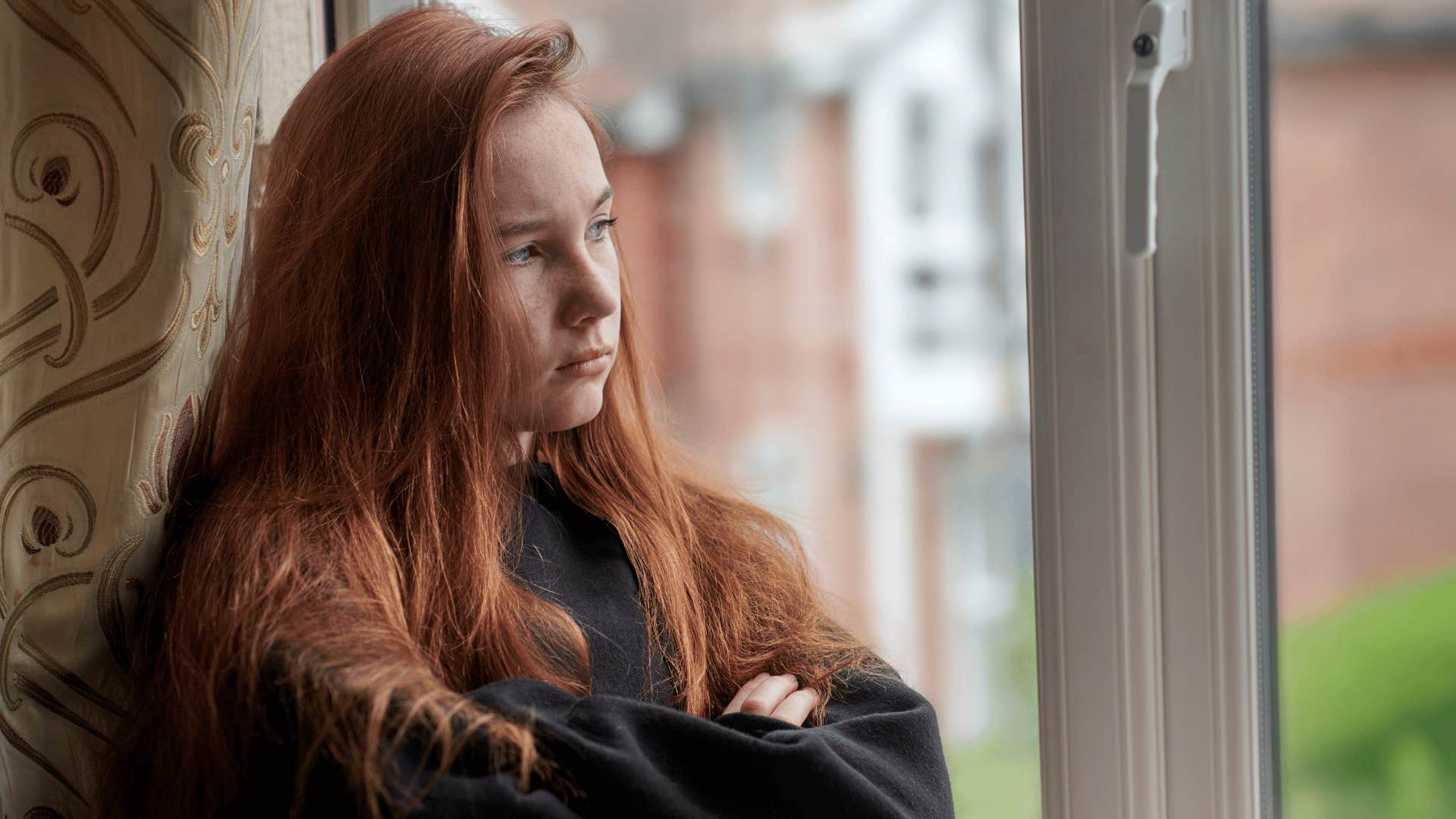 teenage girl with red hair looking out window as she was told to figure it out yourself