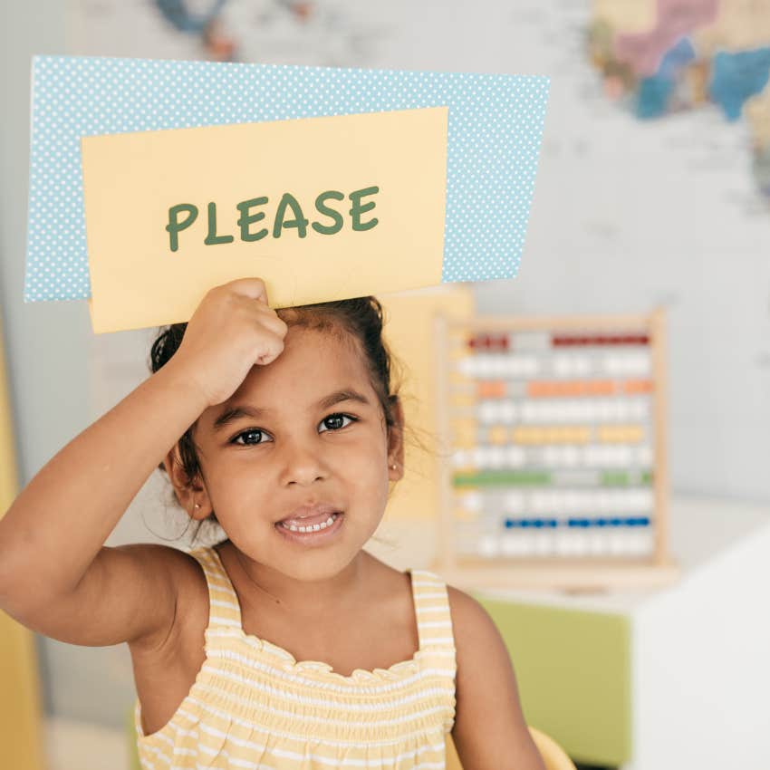 preschool age child holding up a sign that reads "please"