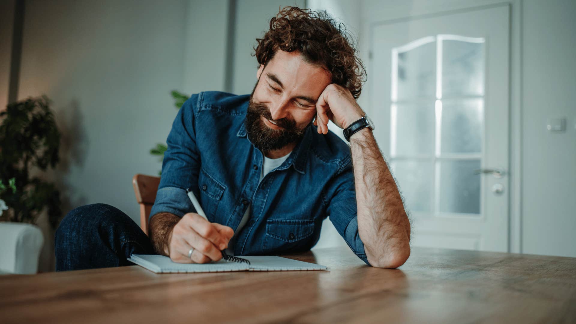 man in blue shirt journaling their thoughts and reflecting on their goals