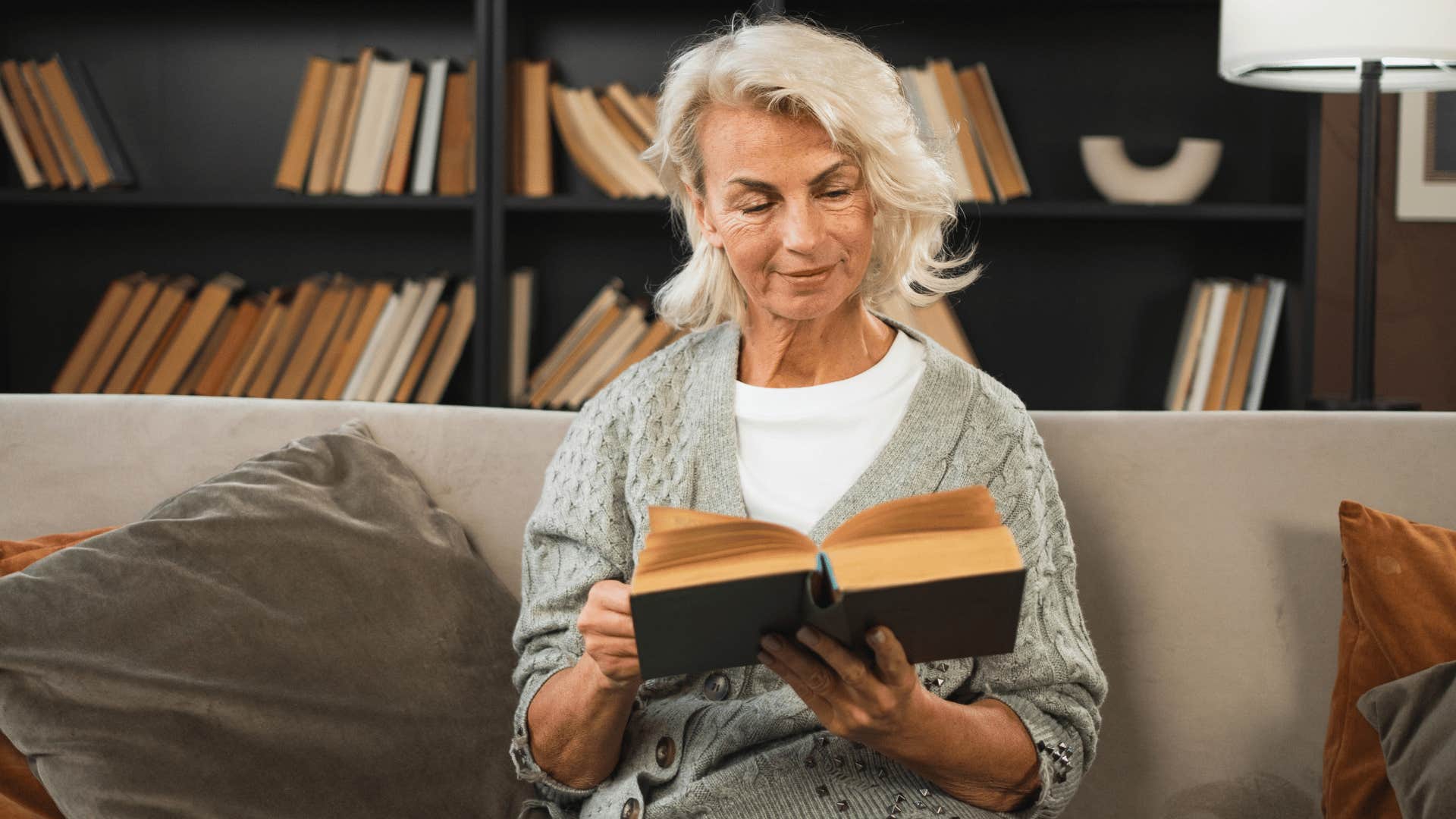 older woman in white shirt reading books as she relaxes on couch