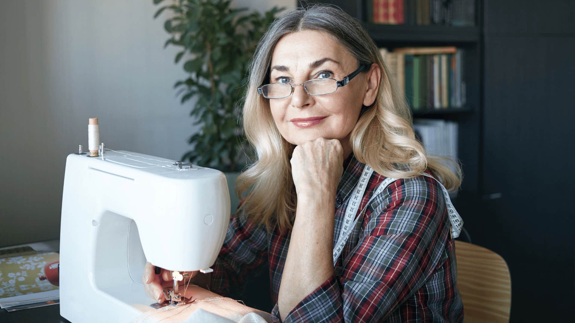 woman in glasses smiling as she is sewing