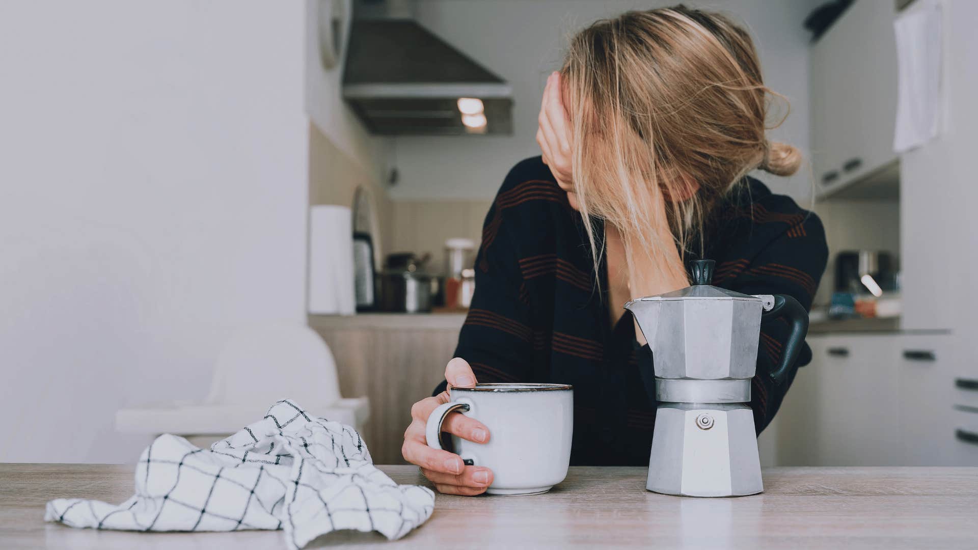 woman clutching head with coffee in hand as she thinks i don't have the energy for this