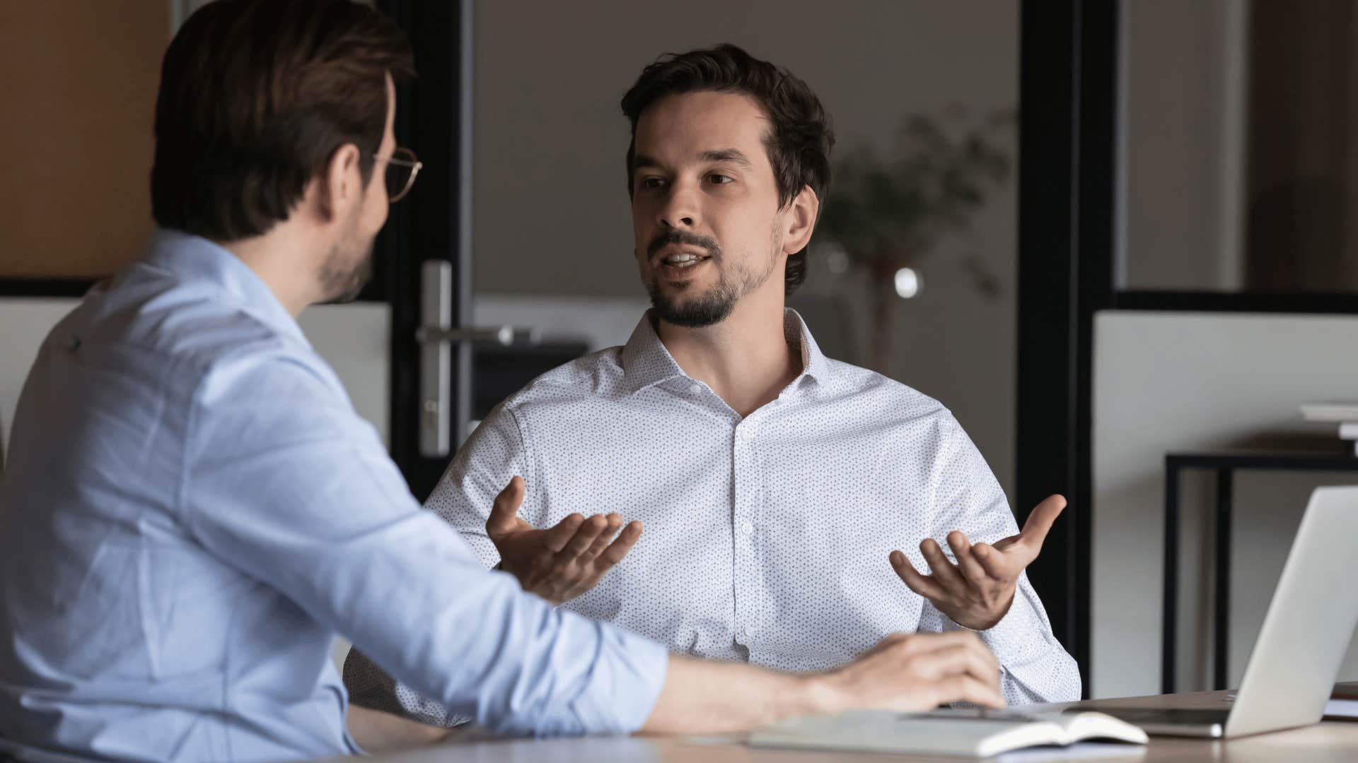 man in white shirt telling coworker i don't want to judge them too harshly