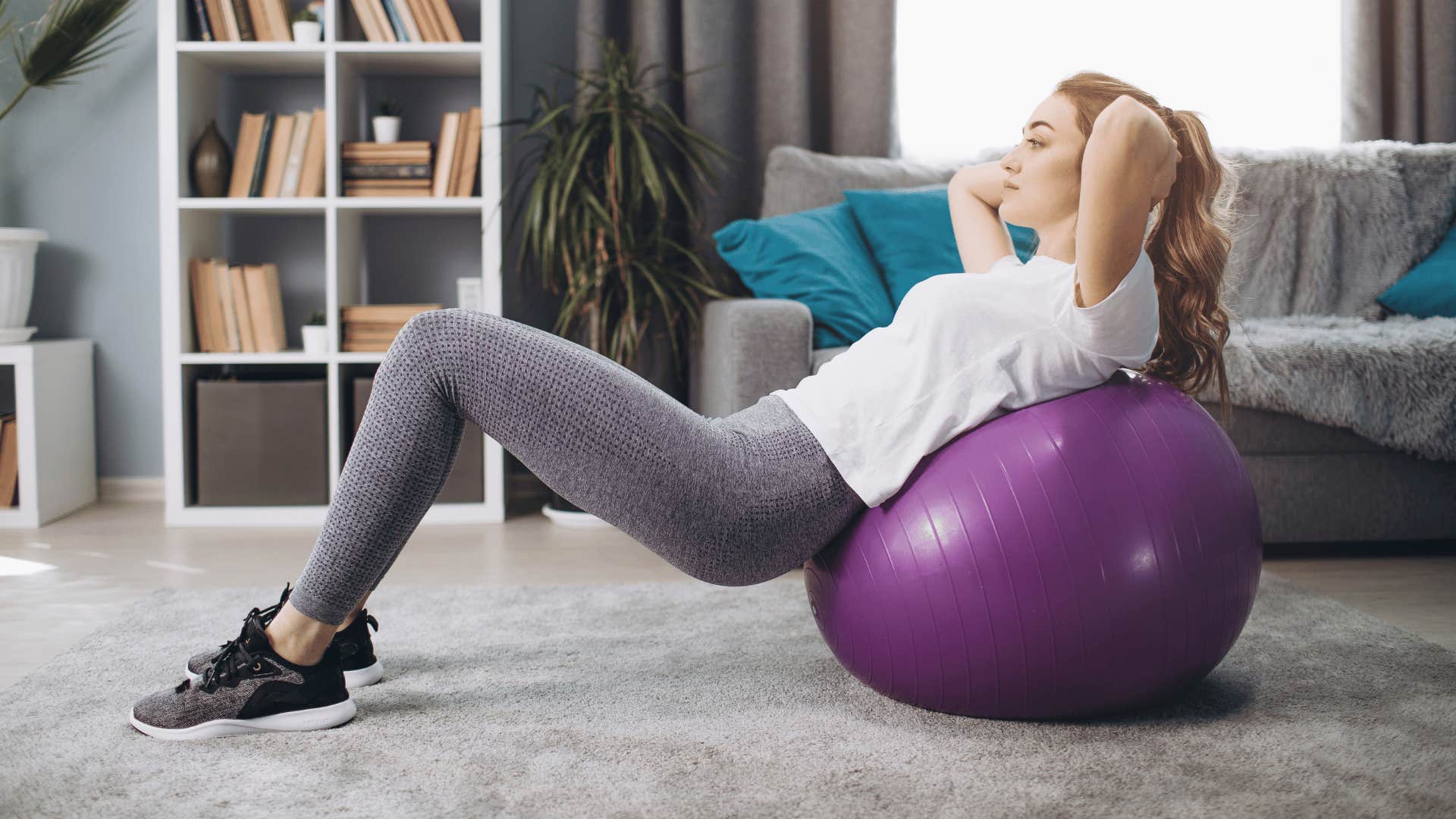 woman with white shirt exercising at home on purple ball