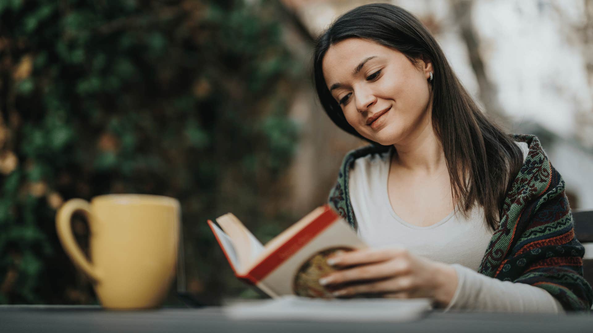 woman reading book outside with yellow mug in front of her