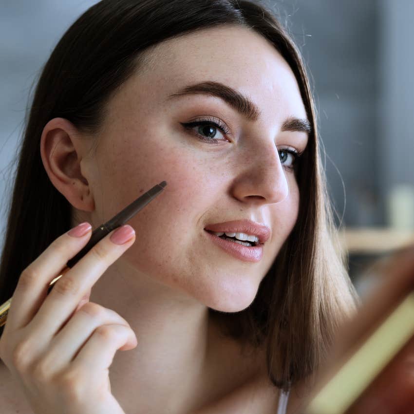 woman putting on fake freckles in her mirror