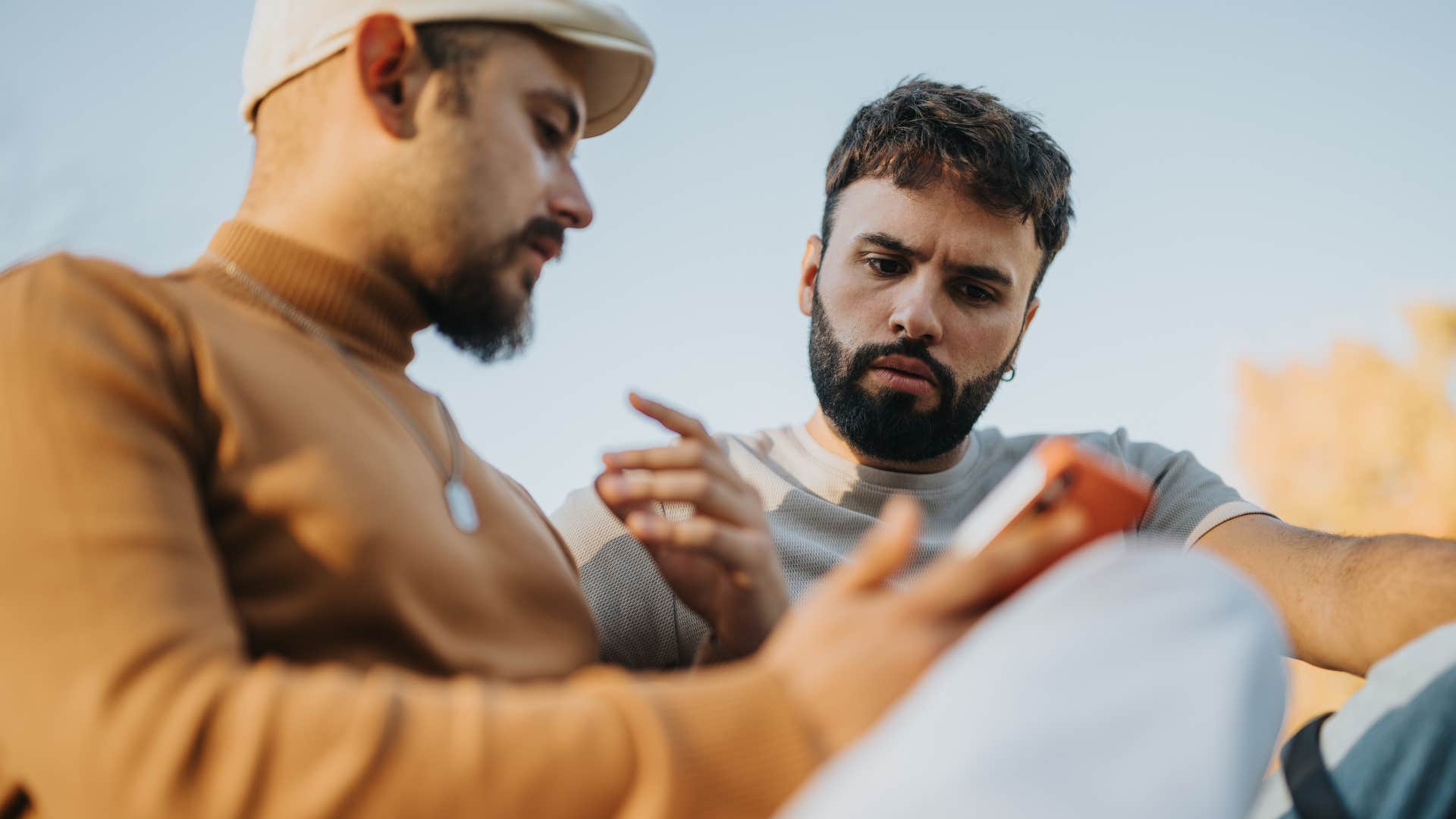 man telling friend he's numb to bad news looking at his phone