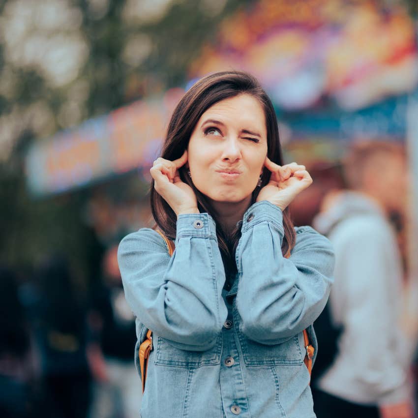 empath woman plugging ears feeling drained at loud packed concert venue
