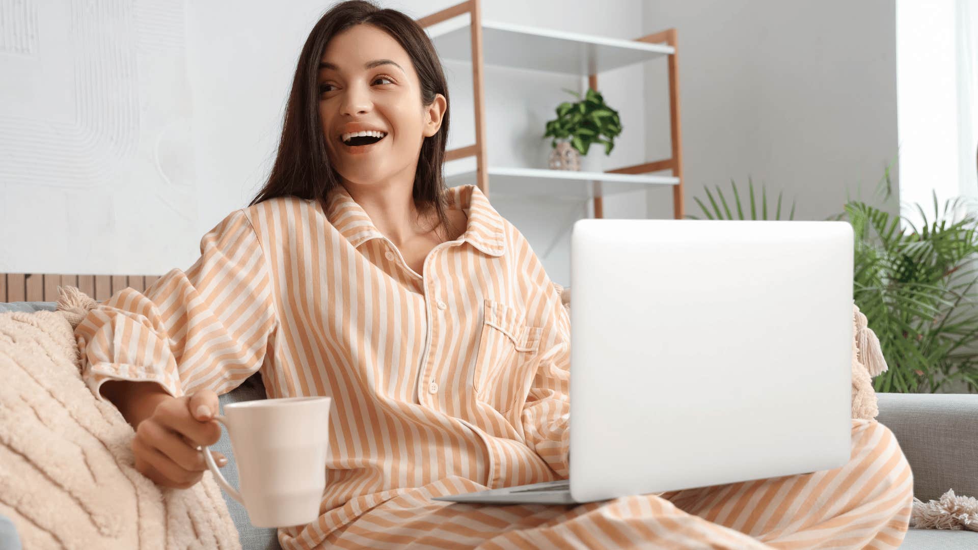 woman working from home in her pajamas as she smiles from the couch