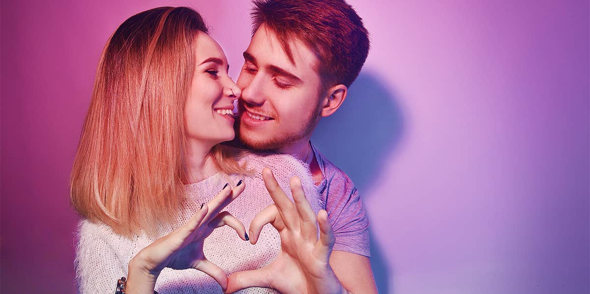man hugging woman from behind making heart shape with their hands