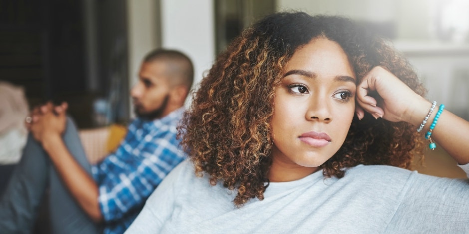 woman looking aimlessly out window with husband in background