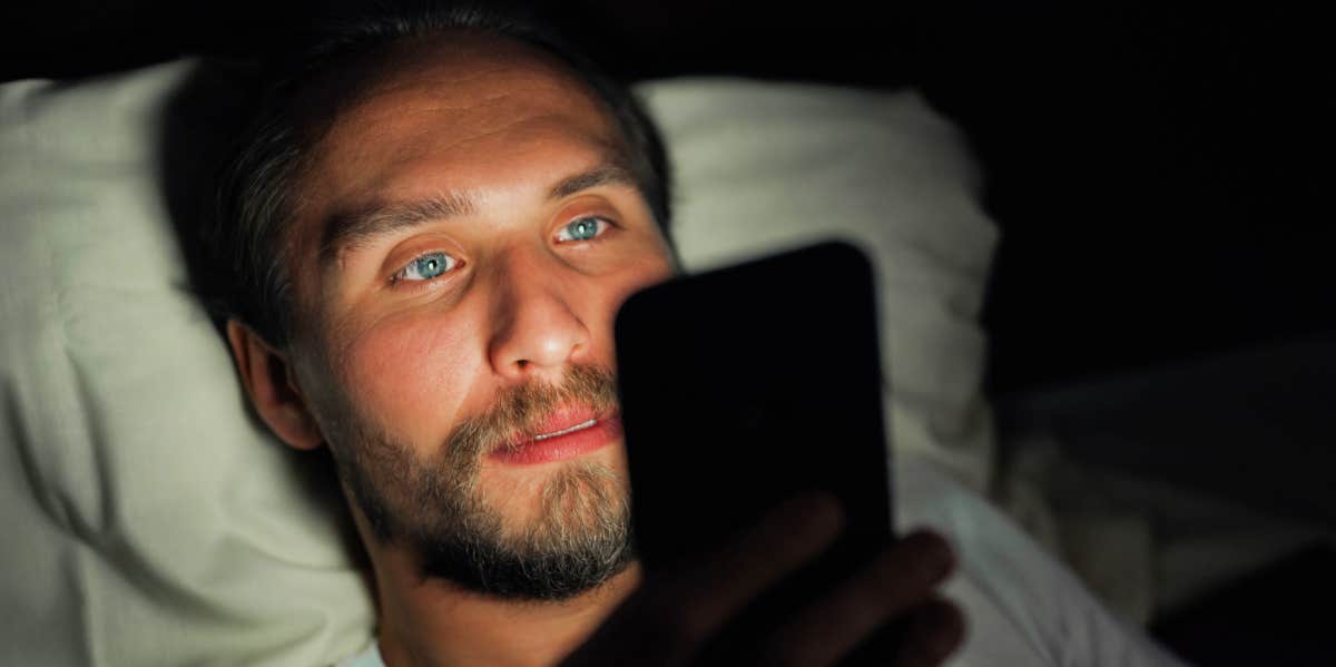 man looking at phone while laying in bed