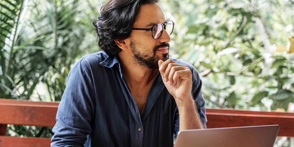 man thinking while writing at laptop