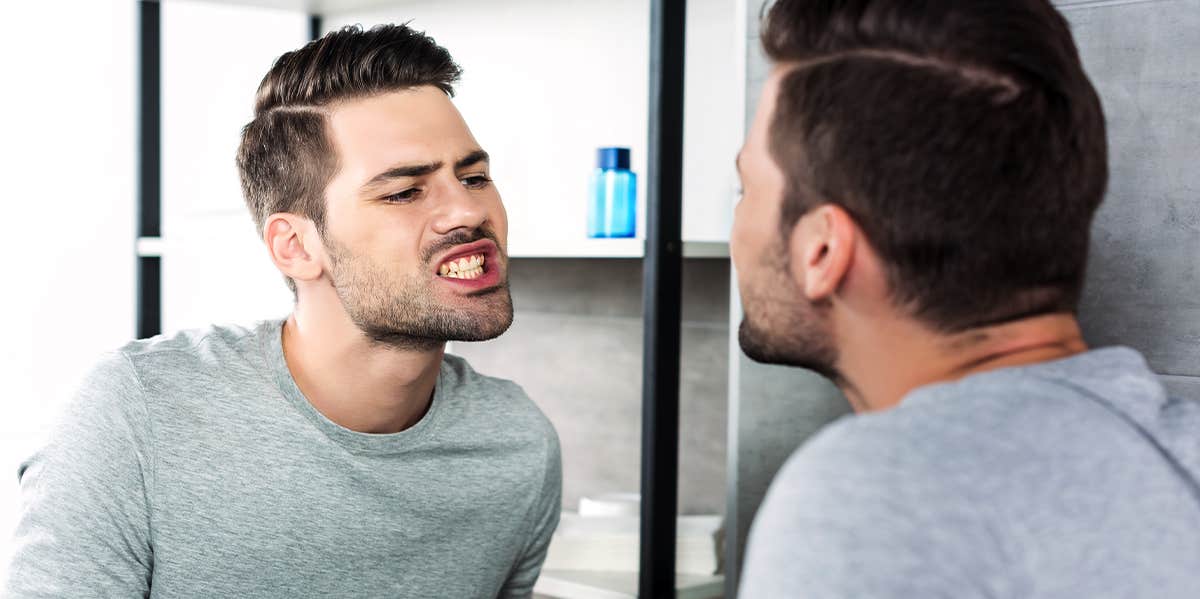 man checking teeth in mirror