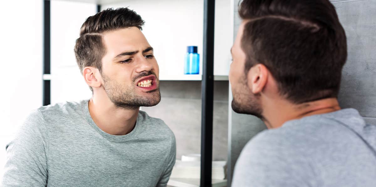 6 Gross Reasons Your Teeth Get Yellow man checking teeth in mirror