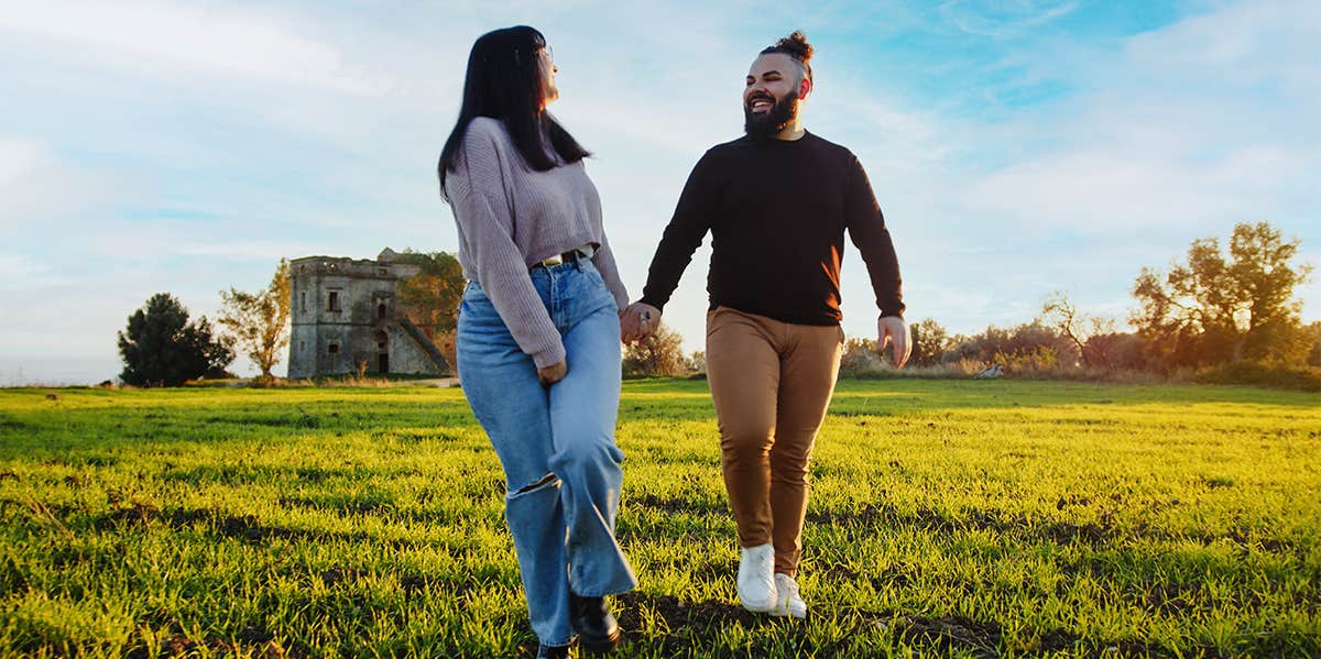 couple holding hands walking in green field