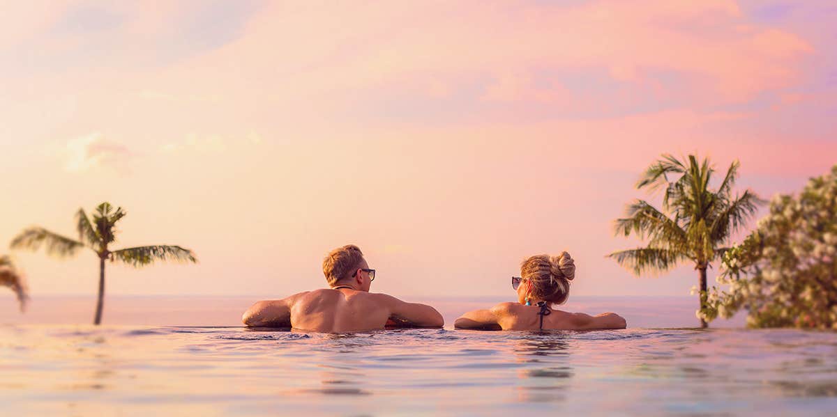 7 Sneaky Ways Traveling Actually Makes You Healthier, Says Science couples in the pool, looking at sunset
